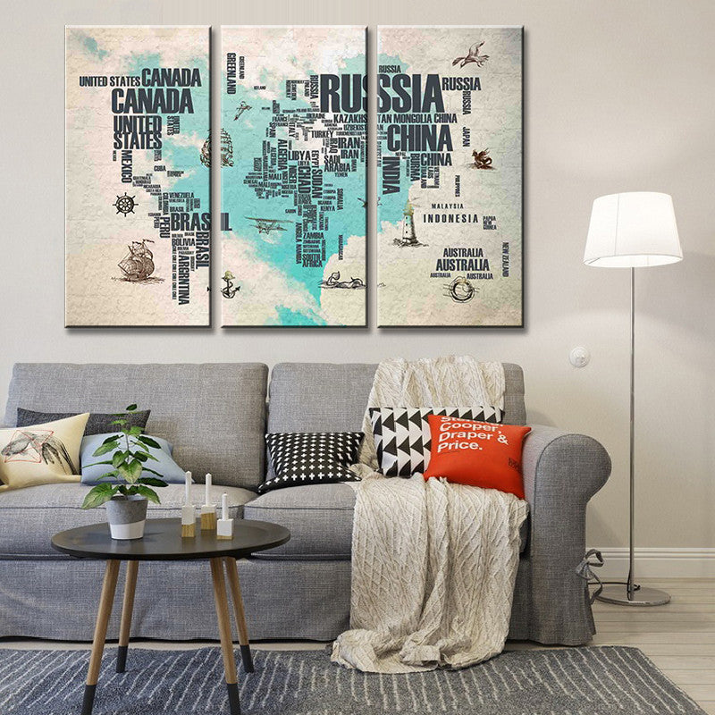 Abstract World Map in Letters - 3-piece canvas wall art featuring world map created with country names in black typography on turquoise watercolor background, displayed above modern gray sofa in contemporary living room setting